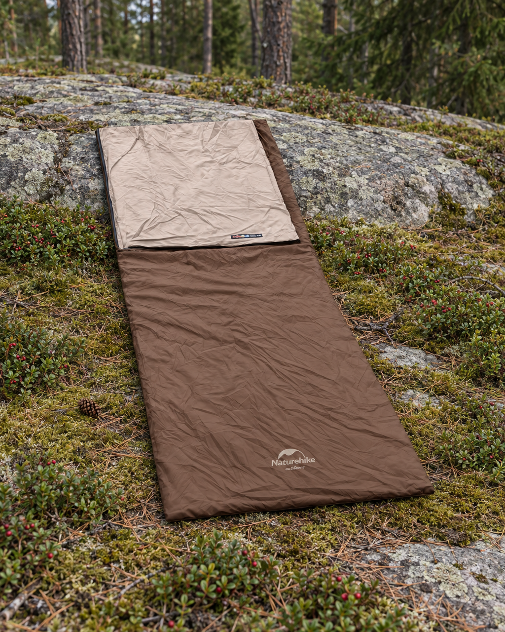 Brown envelope sleeping bag lying open on moss and lingonberry in a forest clearing, head folded back to the beige lining