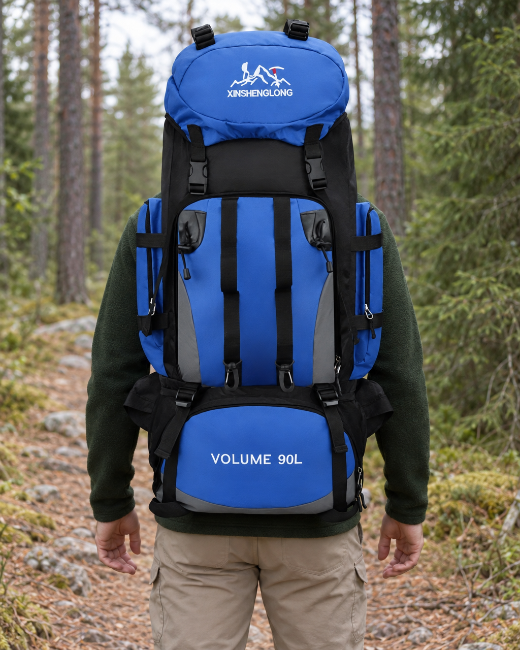 Hiker seen from behind on a forest trail wearing the blue and black 90 L hiking backpack with its hip belt fastened