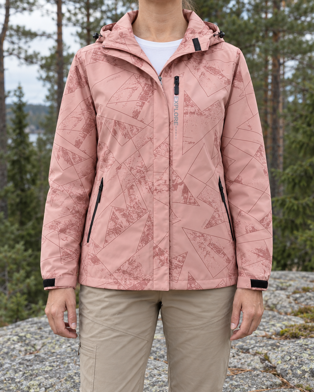 Woman wearing the pink geometric-print hooded hiking jacket zipped up over stone-beige trousers at the forest edge